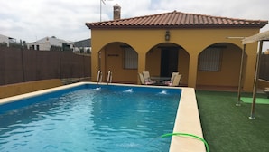 A rectangular swimming pool with a tiled deck, a covered patio with chairs, and a fenced yard. - "Chalet with Pool" (Montellano)