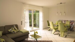 Ein modernes Wohnzimmer mit Sofa, Glastisch und Essbereich mit Tisch und Stühlen.