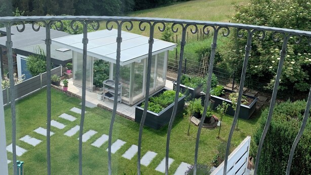 Ein Balkon mit Blick auf einen Garten, ein überdachter Glasbalkon und ein Metallgeländer.