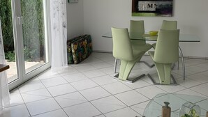 Ein moderner Essbereich mit einem Glastisch, vier Stühlen, einer Couch und einem Glastisch mit einer Schüssel und einer Flasche.