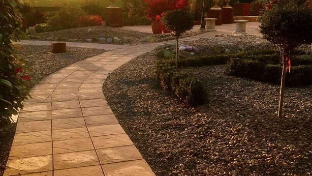 Ein gepflegter Garten mit Topfpflanzen und Bäumen, durch den ein Steinweg führt.