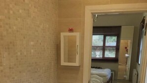 Ein Badezimmer mit gefliesten Wänden, einem Korbstuhl, einer Holzkiste mit Handtüchern und einer Badewanne.