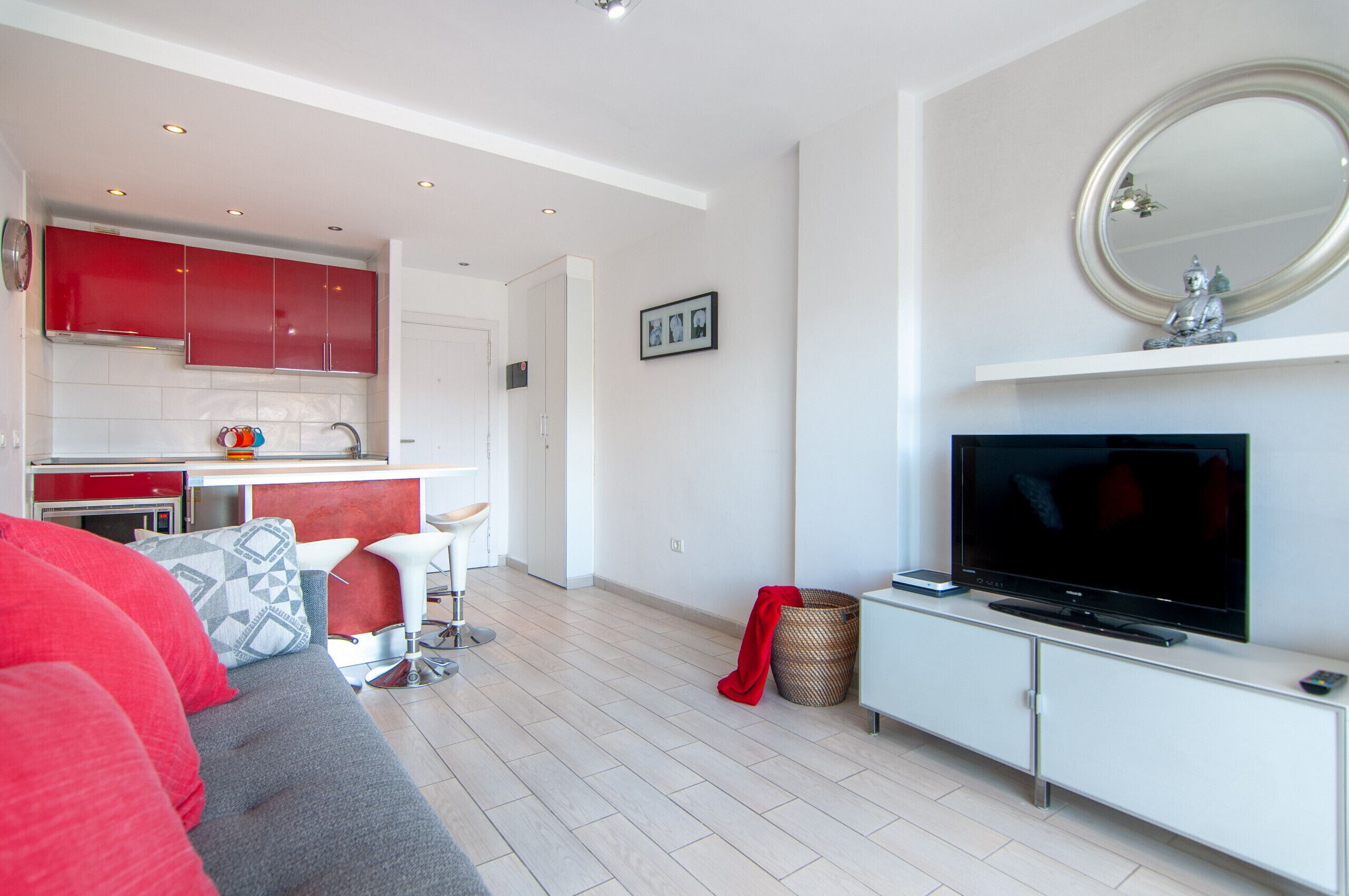 A modern living room with a grey sofa, red cushions, and a TV on a white cabinet.