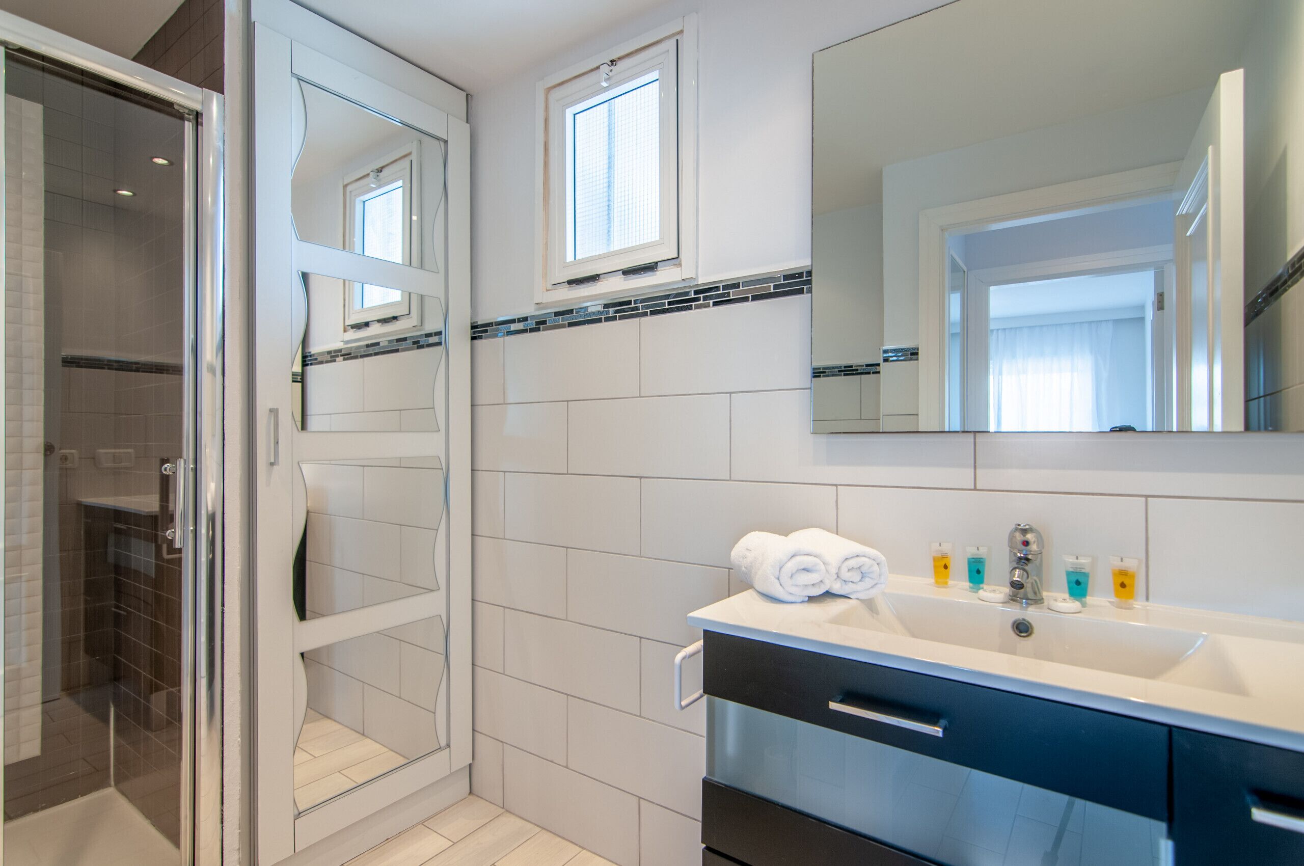 A modern bathroom with a glass shower enclosure, a large mirror, and a vanity with a sink and towel rack.