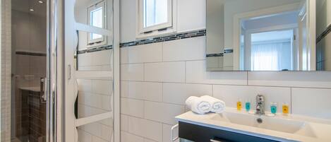 A modern bathroom with a glass shower enclosure, a large mirror, and a vanity with a sink and towel rack.