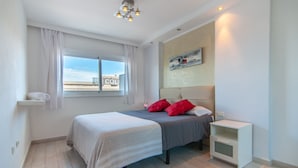 A modern bedroom with a bed, a nightstand, a window with curtains, a ceiling light, and a wall-mounted artwork. - Los Tajinastes 1A034 (Playa de Las Americas)