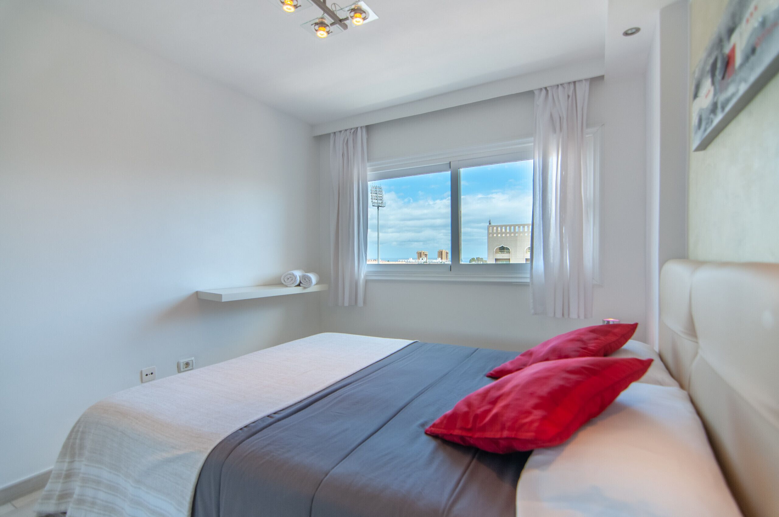 Una camera d'albergo con un letto, una finestra vista città, una lampada a soffitto bianca e un muro bianco.