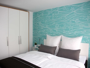 A bedroom with a bed, white and dark grey pillows, and a teal patterned wall.