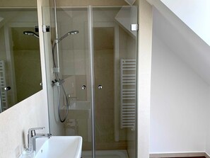 Ein modernes Badezimmer mit einer gläsernen Duschkabine, einem weißen Waschbecken und einem Handtuchhalter.