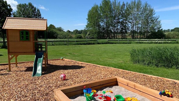 Un parque infantil con un tobogán y una zona de arena llena de juguetes.