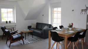 Una sala moderna con un sofá de cuero negro, una mesa de comedor de madera dispuesta para cuatro personas y una alfombra con estampado de cebra.