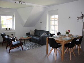 Ein modernes Wohnzimmer mit einer schwarzen Ledersofa, einem Holzesstisch für vier Personen und einem Teppich mit ZEBRA-Muster.