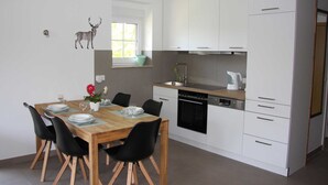 Una cocina moderna con armarios blancos, una mesa de comedor de madera, sillas negras y una ventana pequeña con vistas al verdor.