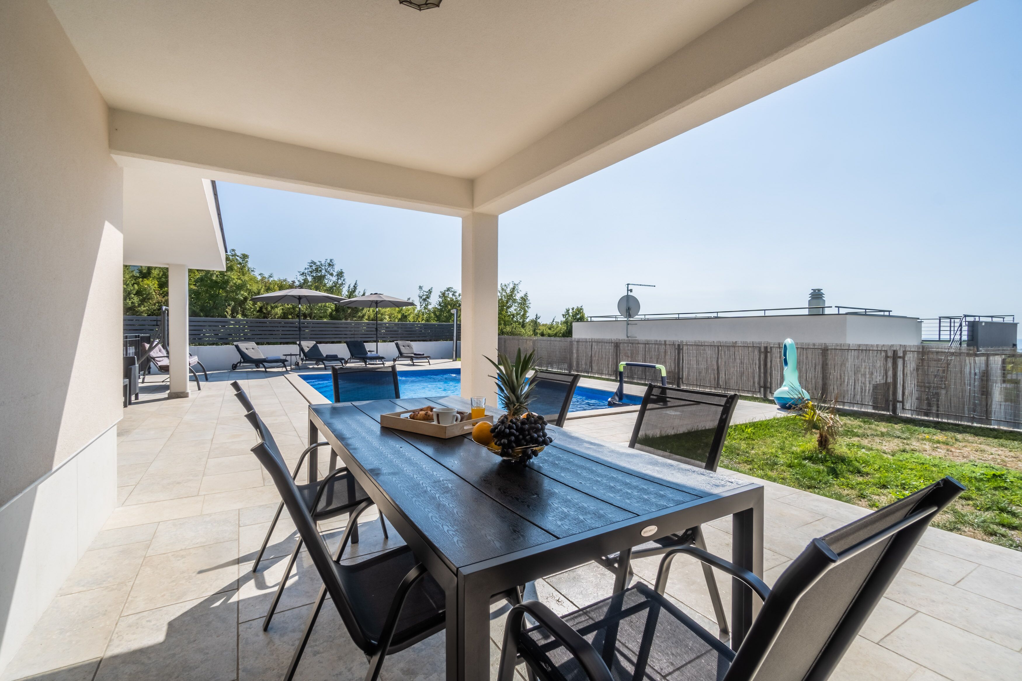 Ein überdachter Patio mit Pool, Sitzgelegenheiten im Freien und einem Tisch mit Obst.