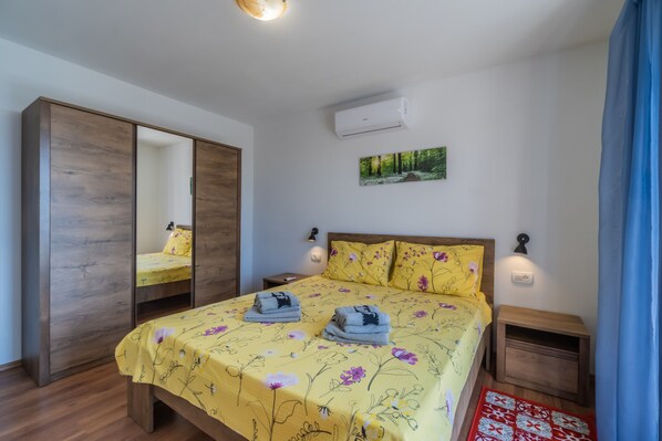 A bedroom with a bed, a wardrobe, a nightstand, and a wall-mounted air conditioner.
