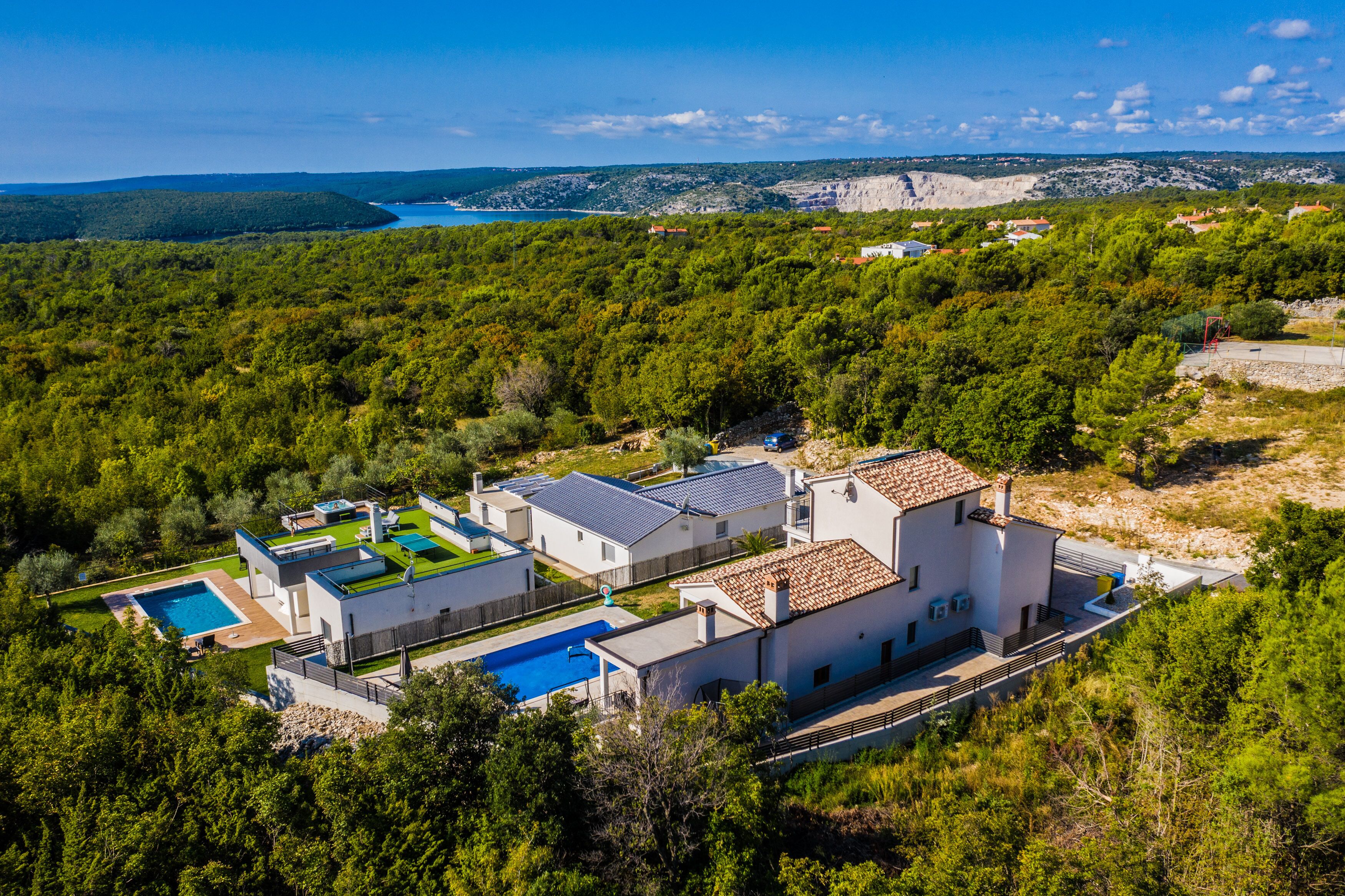 A modern villa with a swimming pool, multiple rooms, and a view of the sea.