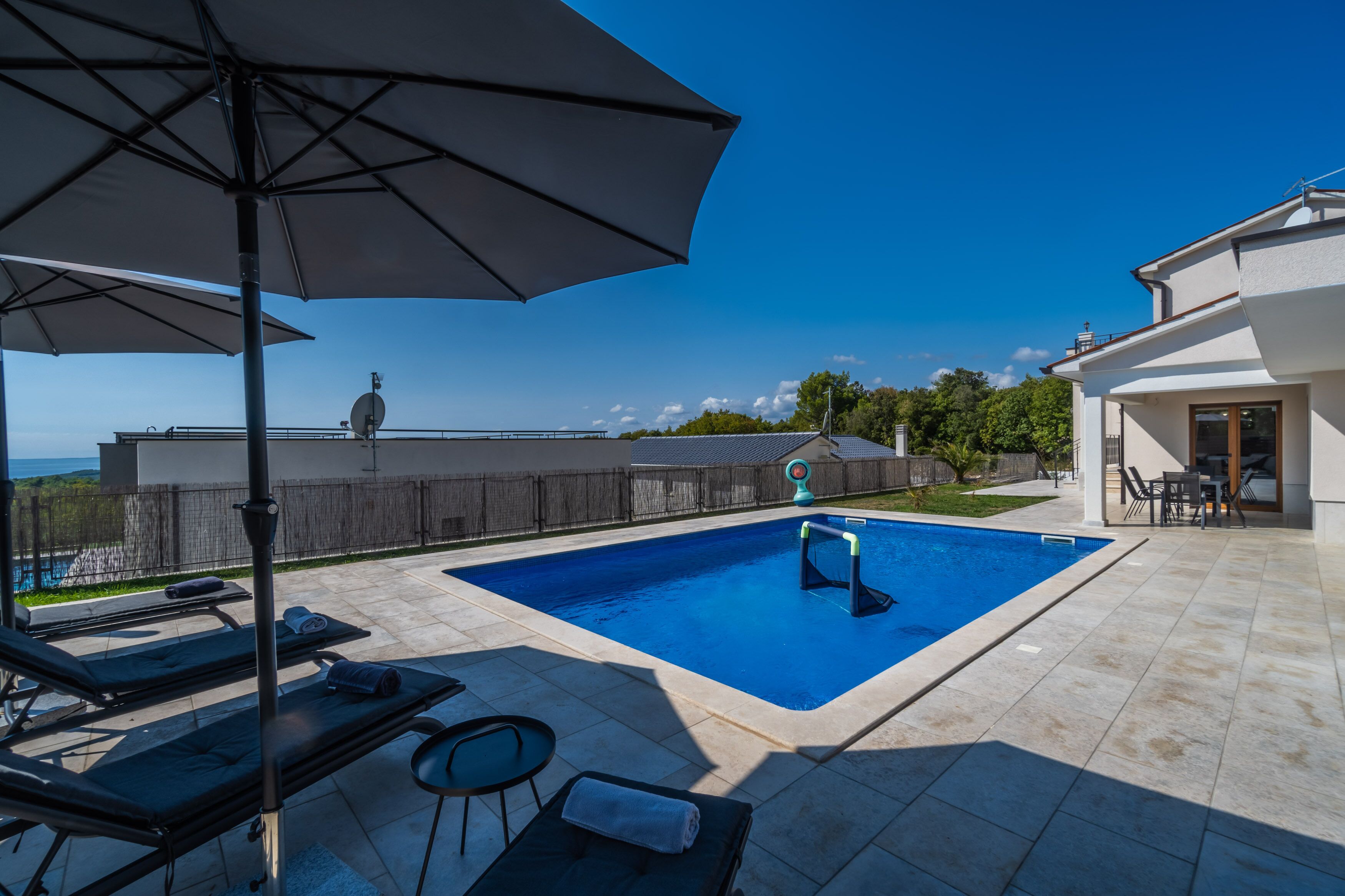A swimming pool with lounge chairs and an umbrella, surrounded by a tiled patio and a view of the sea.