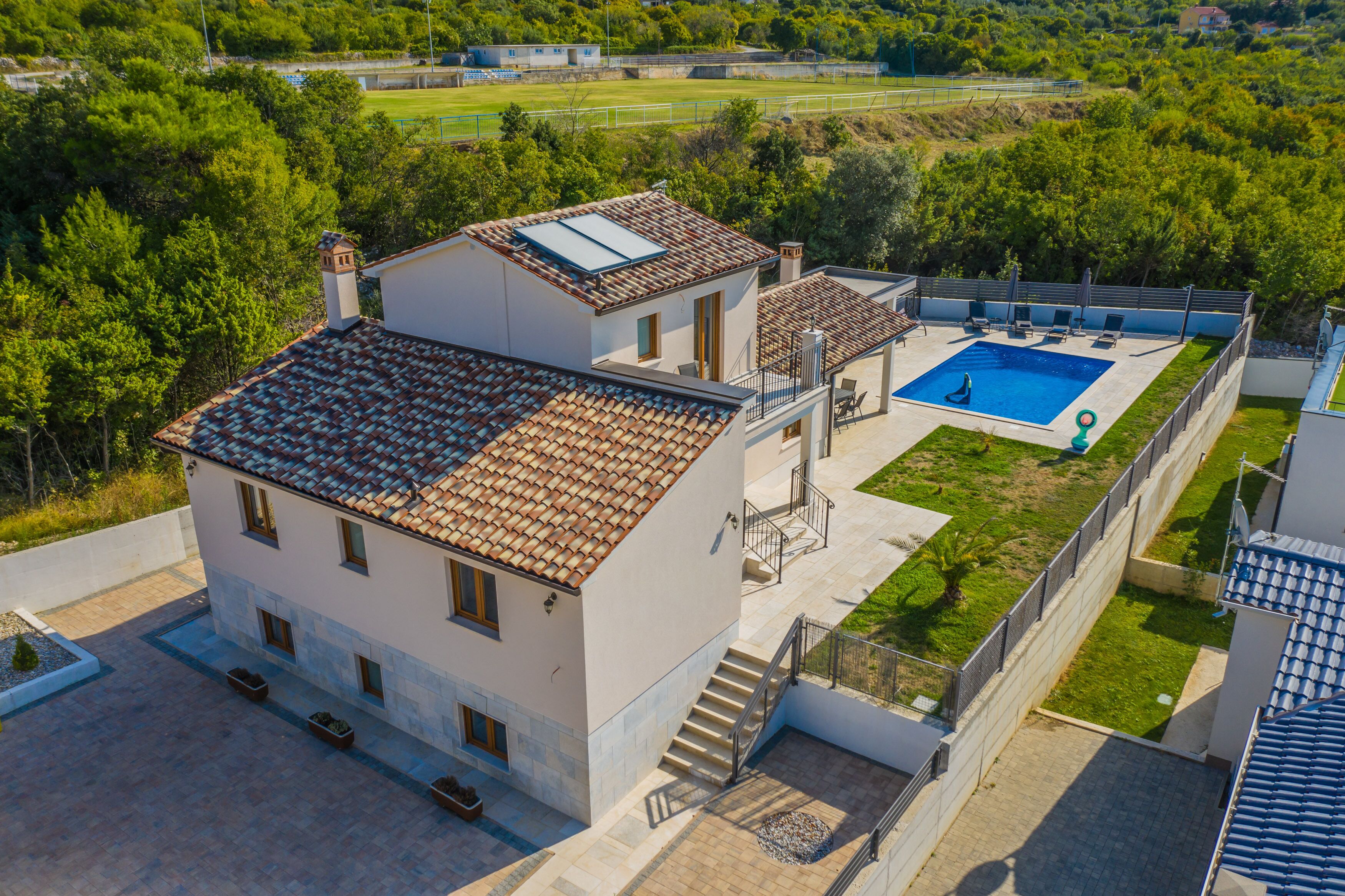 A two-story house with a swimming pool, a covered patio, and a garden.