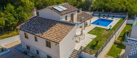 A two-story house with a swimming pool, a covered patio, and a garden.