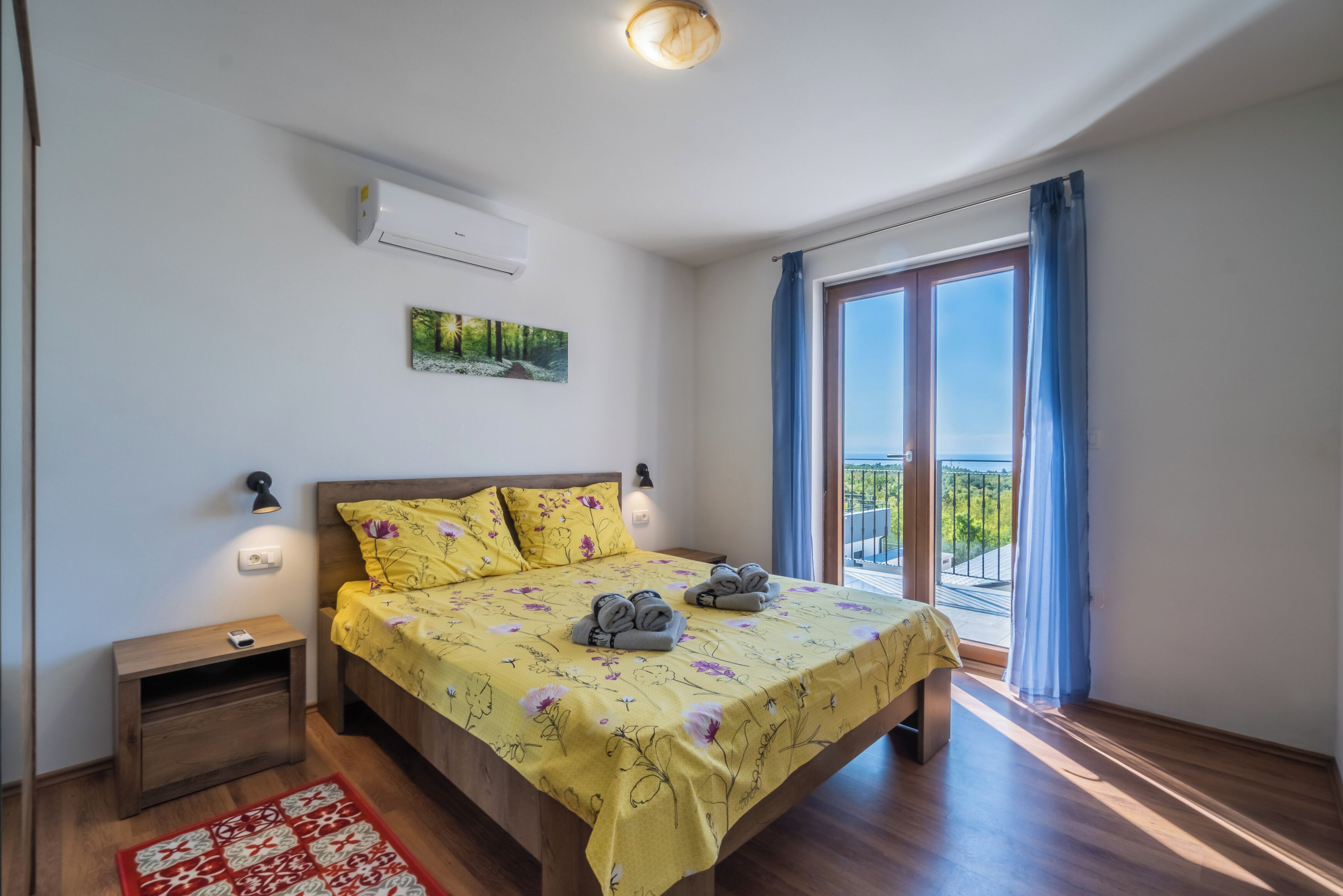 A bedroom with a bed, bedside table, and a view of the outdoors through a window.