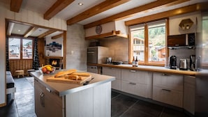 A modern kitchen with wooden beams, a central island, and a view of a village through large windows.