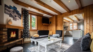 A cozy cabin interior with a fireplace, a sofa, a coffee table, and a kitchen area.