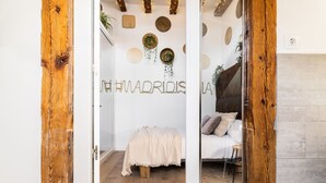 A bedroom with a bed, a wooden floor, and a wall with decorative items and the hashtag #MADRIDISLA.