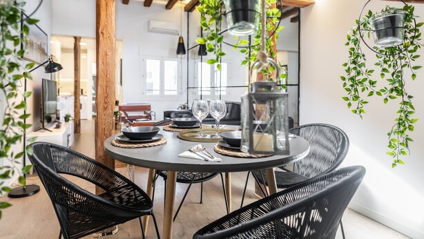A dining area with a round table set for two, surrounded by black wicker chairs.