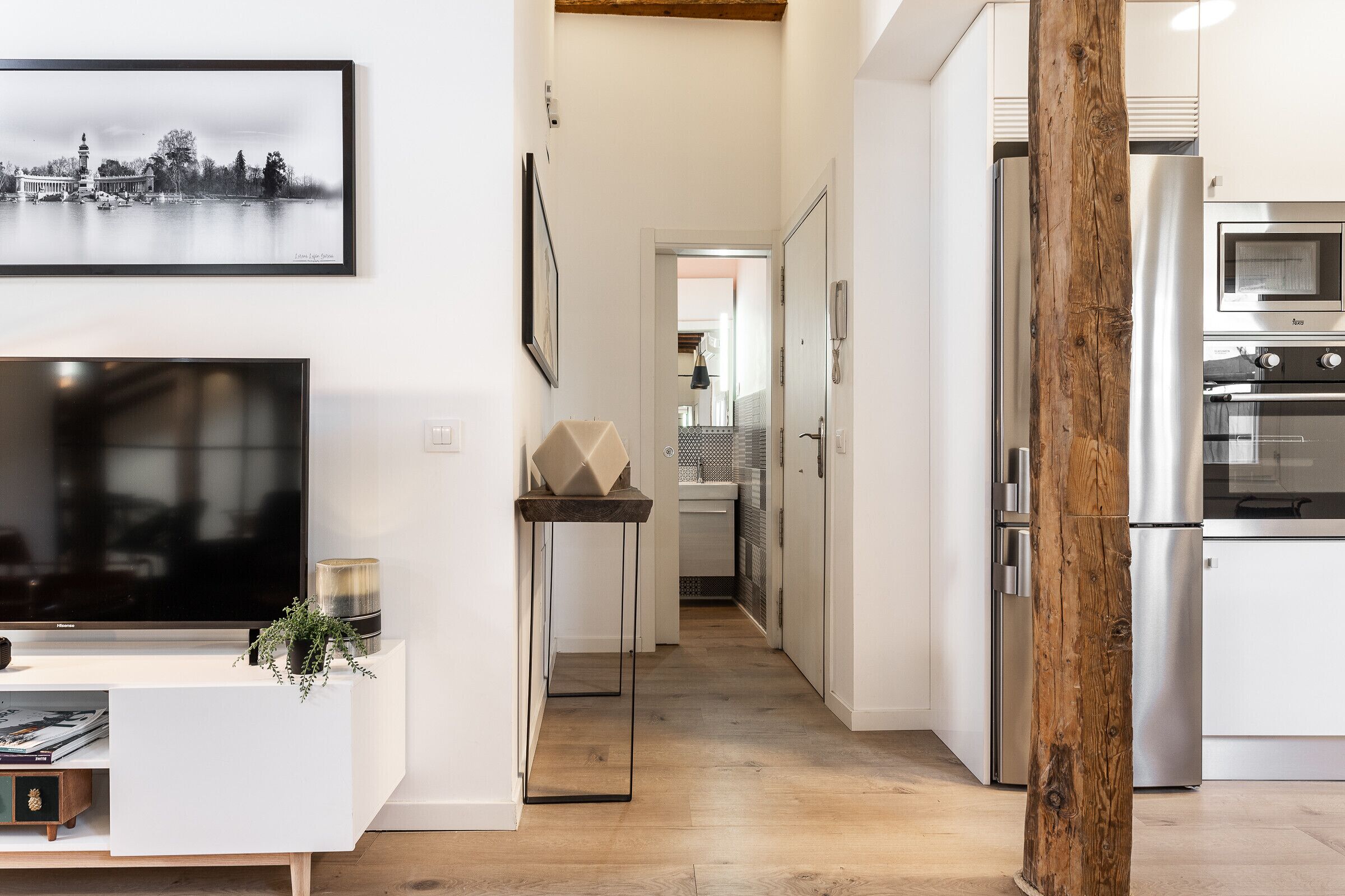 Une cuisine moderne dotée d’appareils électroménagers en acier inoxydable, d’une poutre en bois et d’un tableau représentant un paysage urbain accroché au mur.