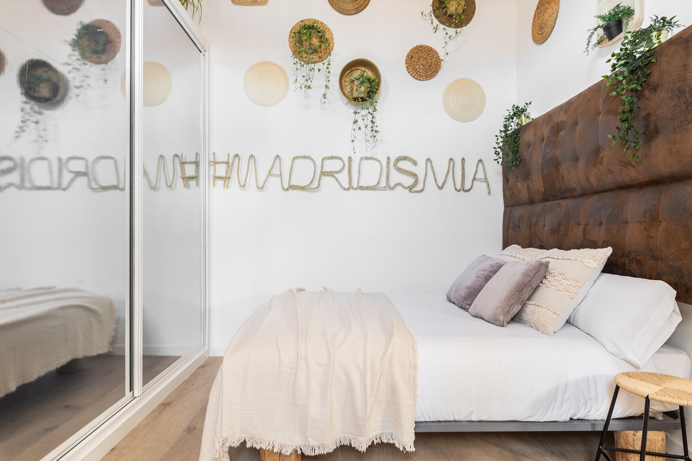 Camera da letto con un letto, un comodino, una pianta sospesa e una parete decorata con elementi quali uno specchio e motivi circolari.