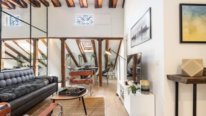 A modern living room with a black leather sofa, wooden beams, a dining area with a table and chairs, and a white console table with a TV.