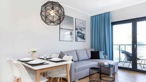 Una sala de estar moderna con comedor, un sofá gris, una mesa de comedor de madera con sillas blancas y una lámpara colgante negra.