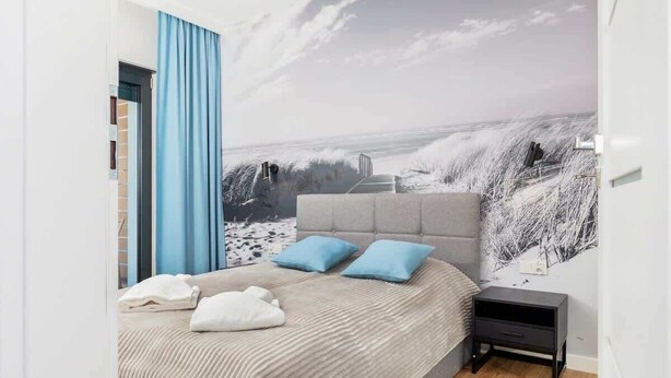 Un dormitorio con una cama grande, una mesita de noche y un mural en la pared con una playa.