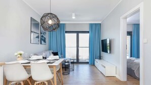 Una sala de estar moderna con comedor, sofá, televisión y un amplio ventanal con cortinas.
