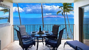 Un balcon avec une table et des chaises, donnant sur une étendue d’eau bordée de palmiers et sur une montagne lointaine.