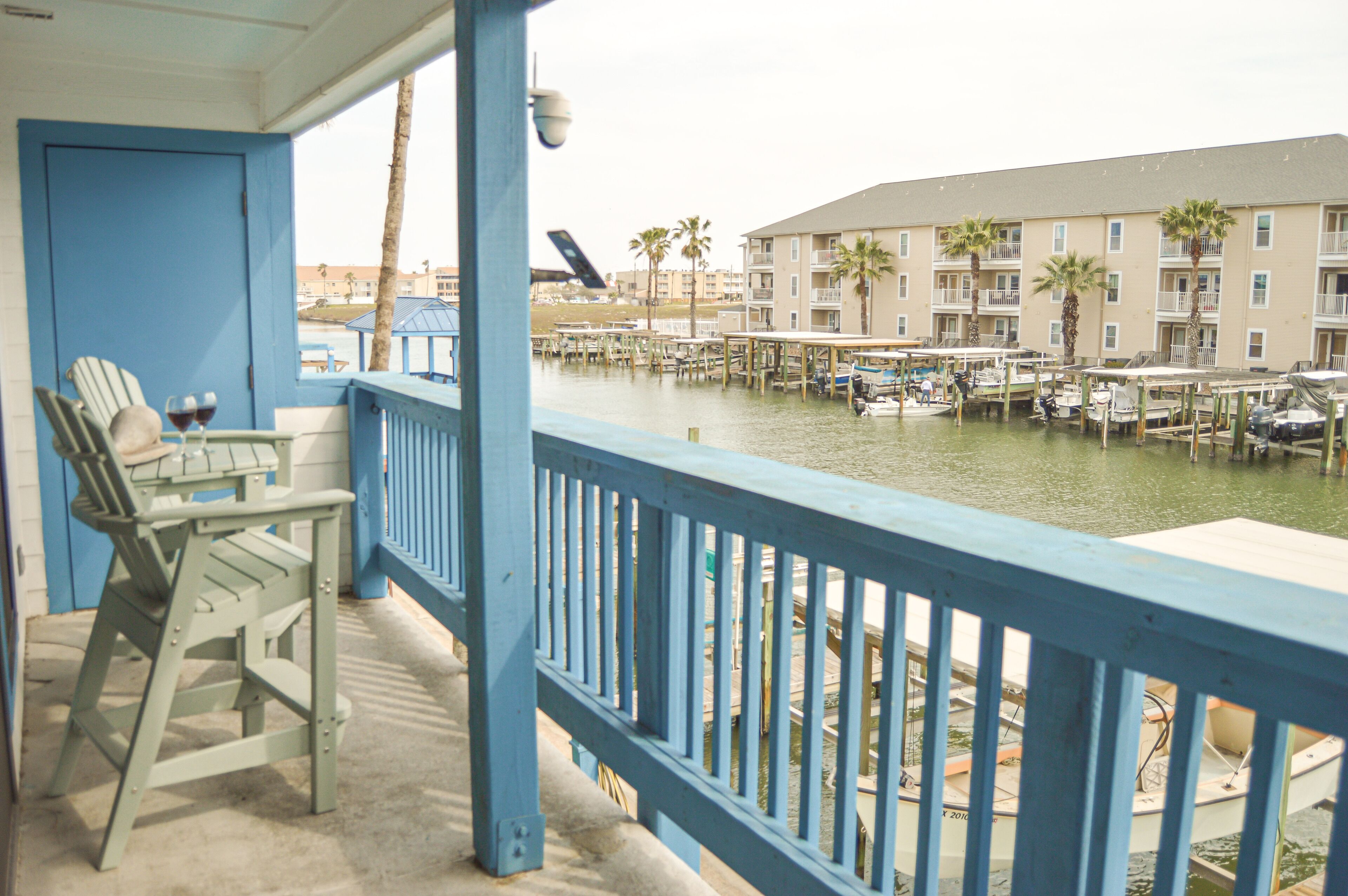 A balcony with chairs and a table, overlooking a marina with boats and a building with balconies.