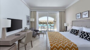 Une chambre d’hôtel avec un lit, un bureau avec une télévision, une chaise, une petite table avec une lampe, et une vue sur une piscine.
