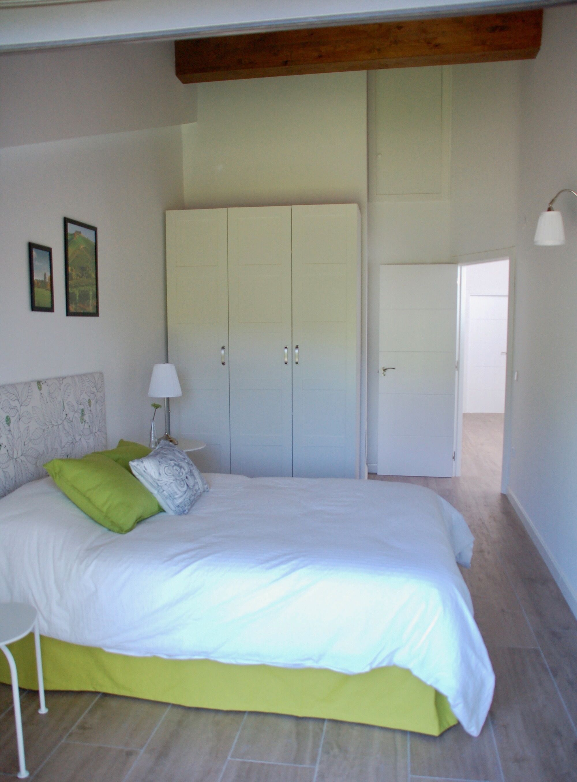A bedroom with a bed, a nightstand, a wardrobe, and a door leading to another room.