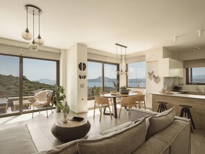 A modern kitchen with large windows, a dining area with a round table, and a living room with a sofa and a coffee table.