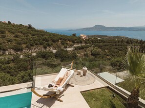 A hammock chair on a terrace overlooking a pool and a mountainous landscape.