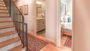Una escalera conduce a un dormitorio con cama, mesita de noche y lámpara.