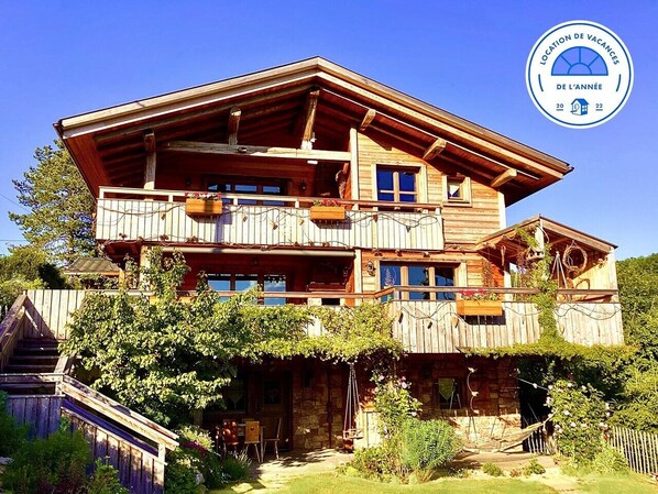 Una cabaña de madera con varios balcones, base de piedra y un jardín rústico.