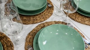 Une table dressée avec des assiettes vertes, des couverts en argent et des verres à vin transparents, le tout posé sur des sets de table en fibres tressées.