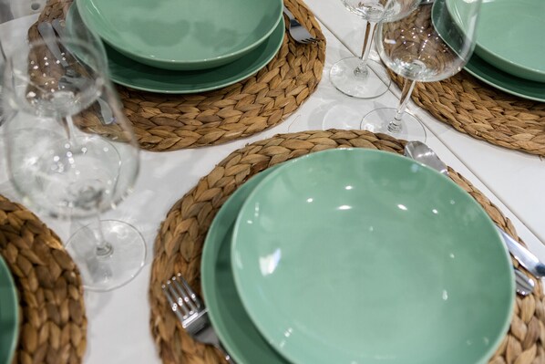 A table set with green plates, silverware, and clear wine glasses on woven placemats.