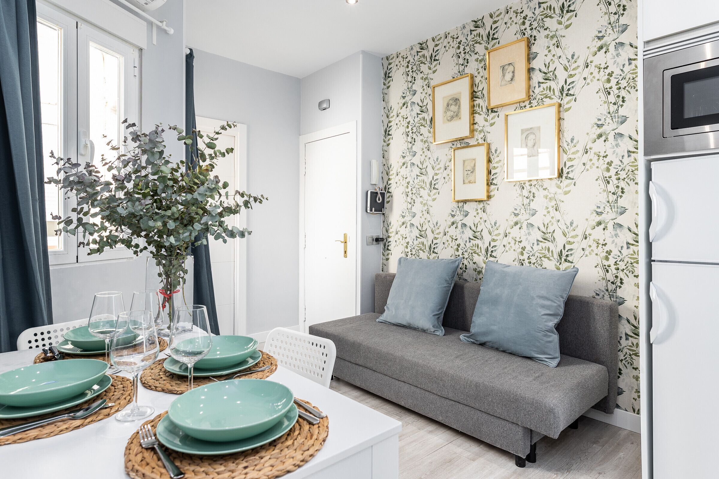 A modern living room with a grey sofa, a dining table set with green plates, and a wall decorated with framed pictures.