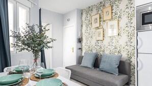 Un salon moderne avec un canapé gris, une table à manger dressée avec de la vaisselle verte et un mur décoré de tableaux encadrés.