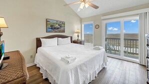 Een slaapkamer met een groot bed, een plafondventilator, een schilderij aan de muur en uitzicht op de omgeving door een schuifdeur met glas.