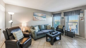 A living room with a sofa, armchair, and coffee table. There is a painting on the wall and a lamp on the side table. - Dog-Friendly Beachside Retreat | Patio, Pool & Hot Tub (Corpus Christi)