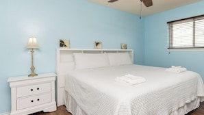 A bedroom with a bed, a nightstand, a lamp, a ceiling fan, and a window with blinds. - Steps to Beach & Pool | Easy Coastal Getaway (Corpus Christi)
