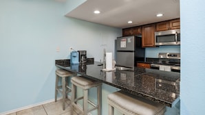 A kitchen with light blue walls, dark granite countertops, stainless steel appliances, and wooden cabinets. - Steps to Beach & Pool | Easy Coastal Getaway (Corpus Christi)